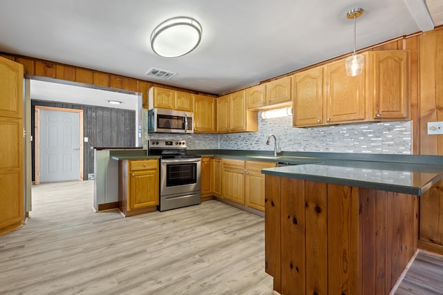 kitchen featuring kitchen peninsula, appliances with stainless steel finishes, decorative backsplash, light hardwood / wood-style floors, and hanging light fixtures