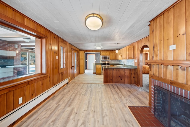 kitchen with stainless steel appliances, a baseboard radiator, pendant lighting, light hardwood / wood-style floors, and wooden walls