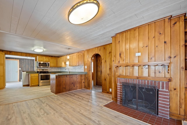 kitchen with kitchen peninsula, stainless steel appliances, decorative light fixtures, light hardwood / wood-style flooring, and wood walls