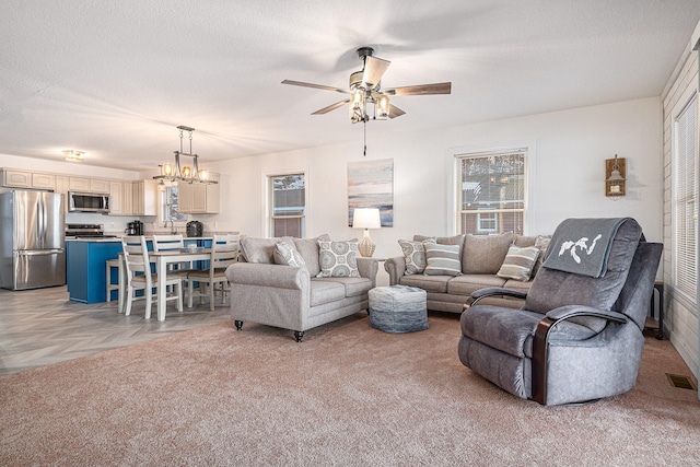 living room with ceiling fan with notable chandelier, a textured ceiling, and light carpet