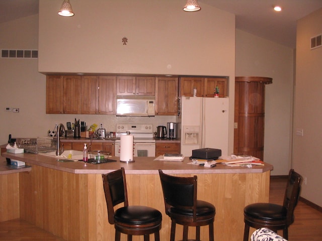 kitchen featuring wood-type flooring, lofted ceiling, a breakfast bar area, and white appliances