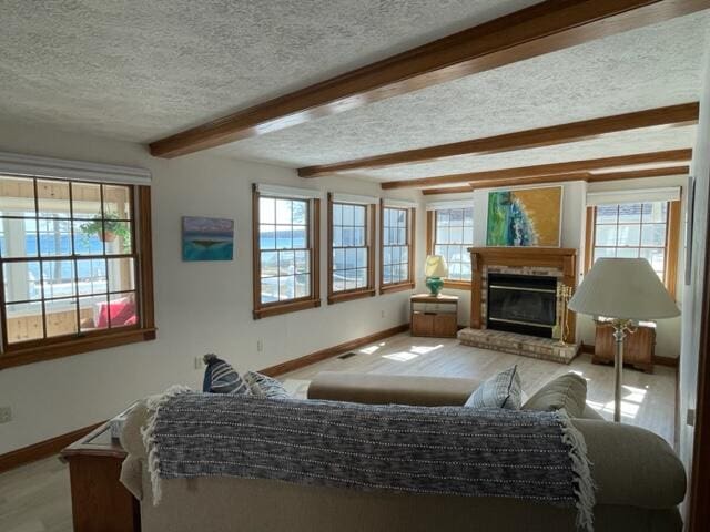 living room with beamed ceiling, plenty of natural light, a fireplace, and a textured ceiling