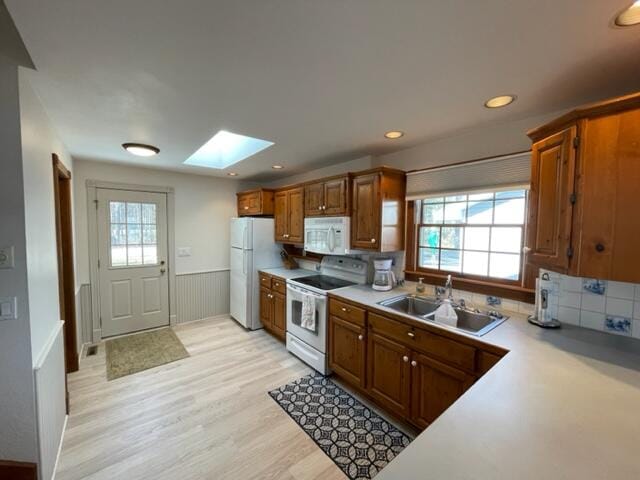 kitchen featuring a skylight, white appliances, sink, and a healthy amount of sunlight