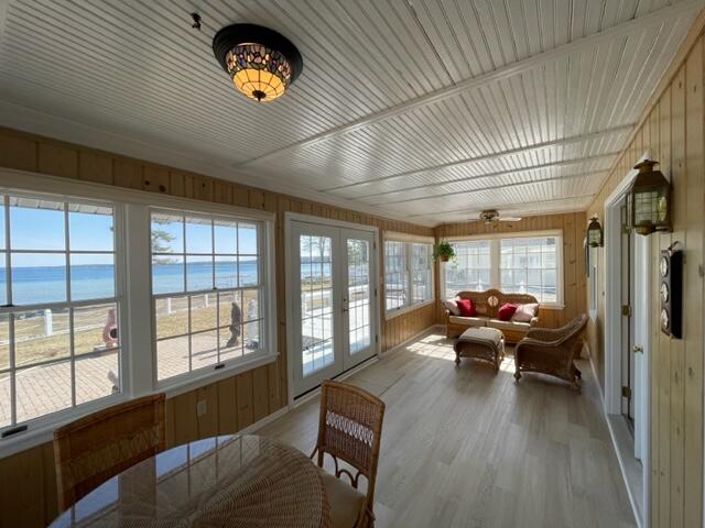 sunroom with french doors, a water view, ceiling fan, and a view of the beach