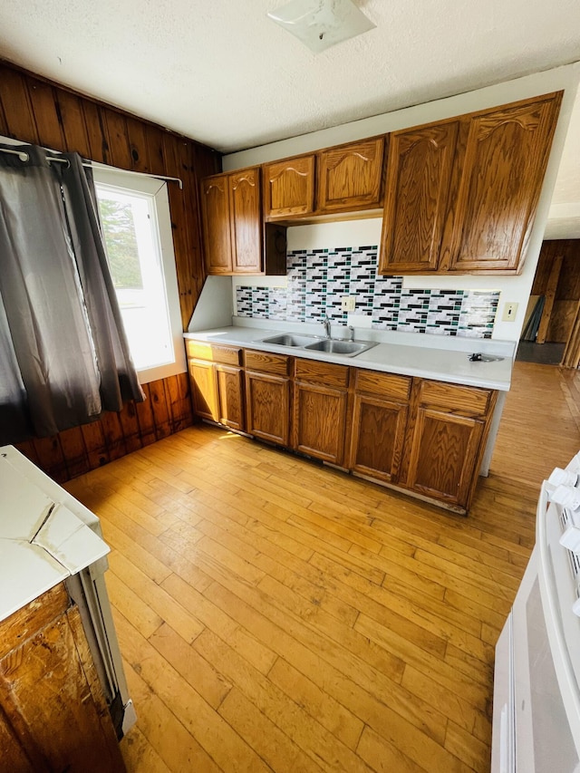 kitchen featuring wooden walls, white stove, light hardwood / wood-style flooring, sink, and decorative backsplash