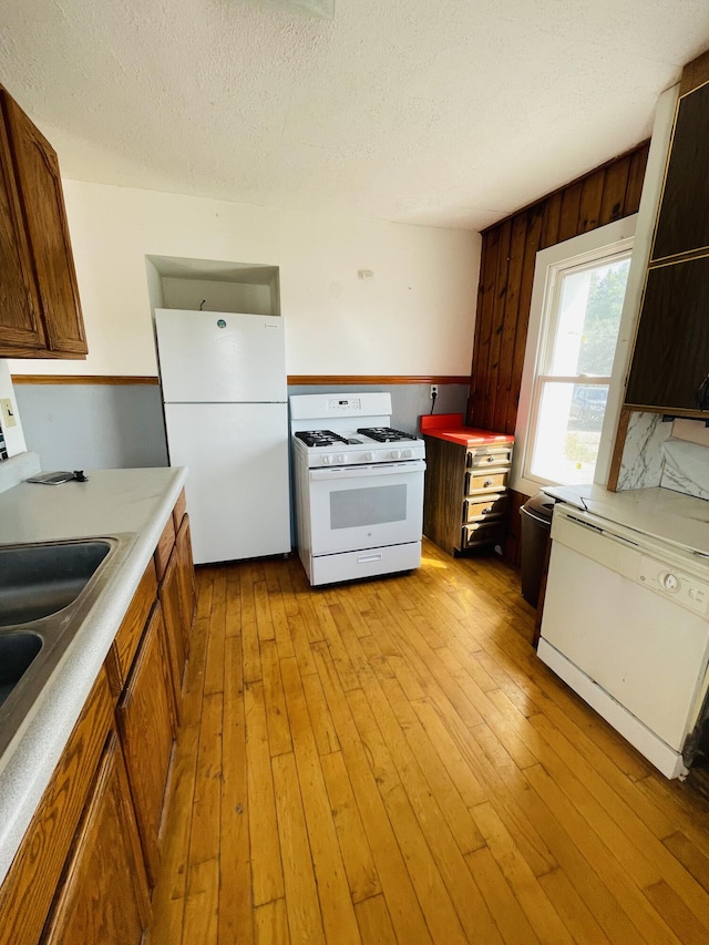 kitchen with light wood-type flooring, white appliances, sink, wood walls, and a textured ceiling