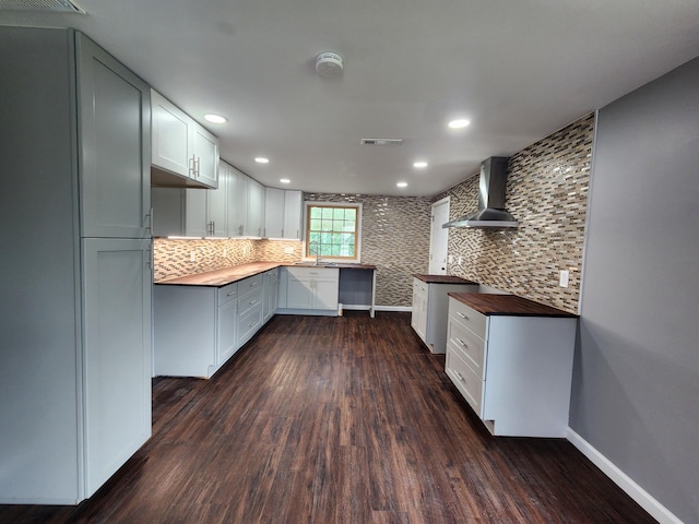 kitchen with butcher block countertops, tasteful backsplash, wall chimney range hood, dark hardwood / wood-style floors, and white cabinetry