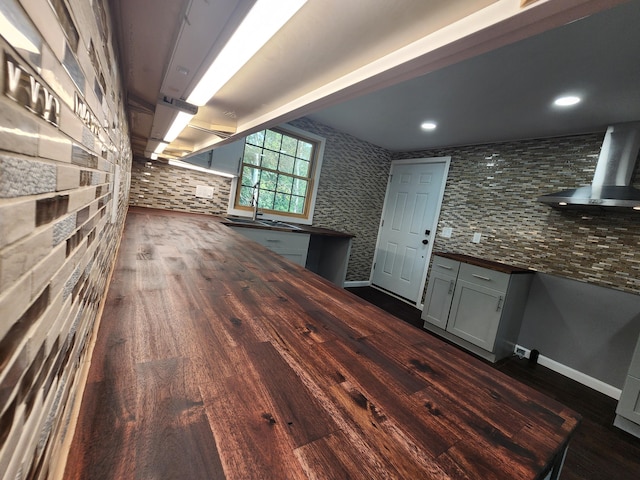 interior space featuring dark hardwood / wood-style flooring, tasteful backsplash, and wall chimney range hood