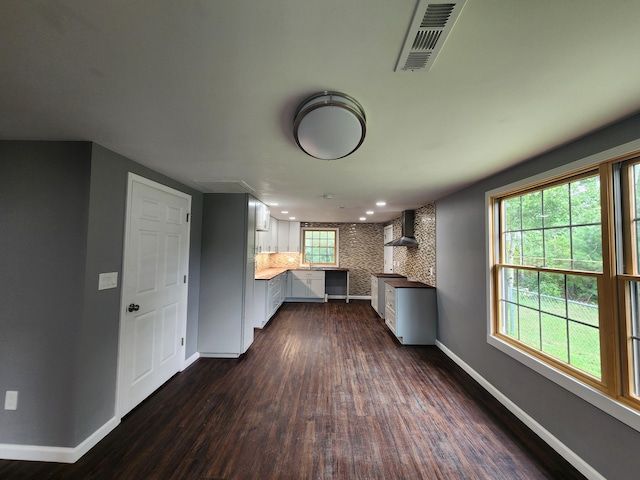 interior space featuring kitchen peninsula, white cabinets, backsplash, dark wood-type flooring, and wall chimney exhaust hood