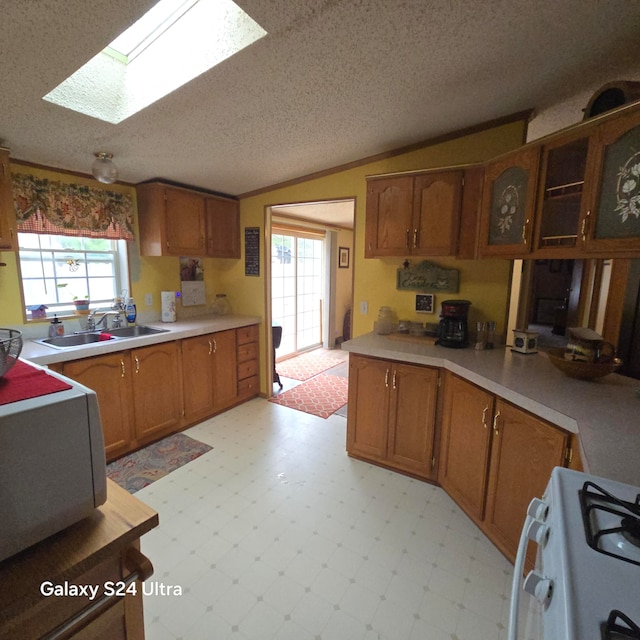 kitchen with range, light tile floors, vaulted ceiling with skylight, a textured ceiling, and sink