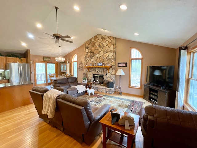 living room with a stone fireplace, ceiling fan with notable chandelier, light hardwood / wood-style flooring, and lofted ceiling