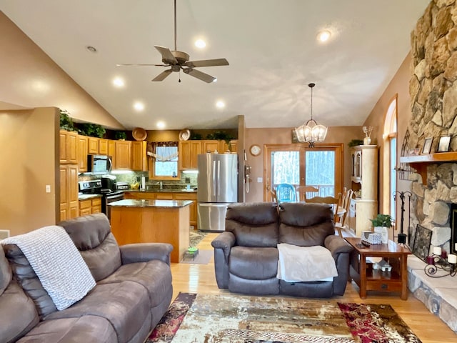 living room featuring vaulted ceiling, light hardwood / wood-style flooring, a fireplace, ceiling fan with notable chandelier, and sink