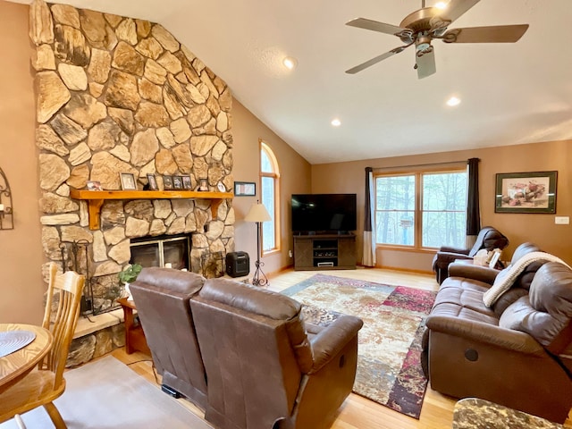 living room featuring a stone fireplace, ceiling fan, vaulted ceiling, and light wood-type flooring