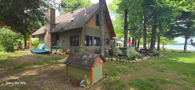 rear view of property with a storage unit, a lawn, and a water view