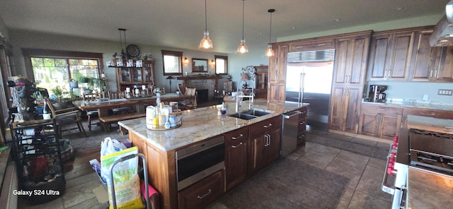 kitchen featuring sink, a brick fireplace, stainless steel appliances, pendant lighting, and a center island with sink