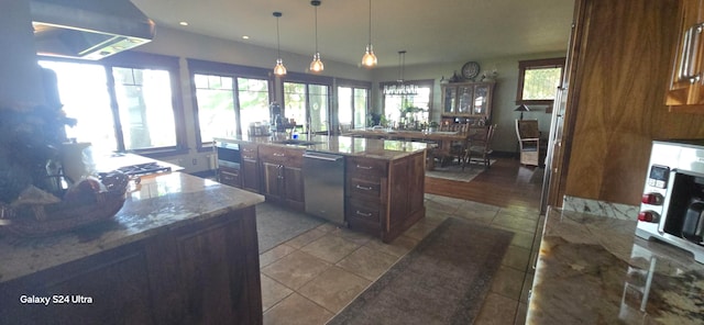 kitchen with stainless steel dishwasher, a kitchen island with sink, hanging light fixtures, and a healthy amount of sunlight