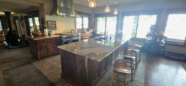 kitchen featuring sink, hanging light fixtures, wall chimney exhaust hood, a breakfast bar, and double oven range