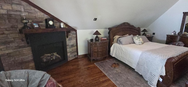 bedroom featuring a stone fireplace, vaulted ceiling, and dark hardwood / wood-style floors