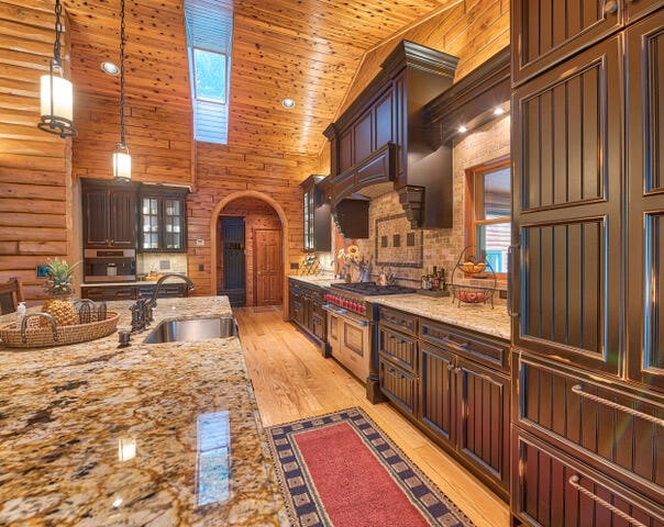 kitchen featuring light wood-type flooring, decorative light fixtures, high vaulted ceiling, sink, and rustic walls