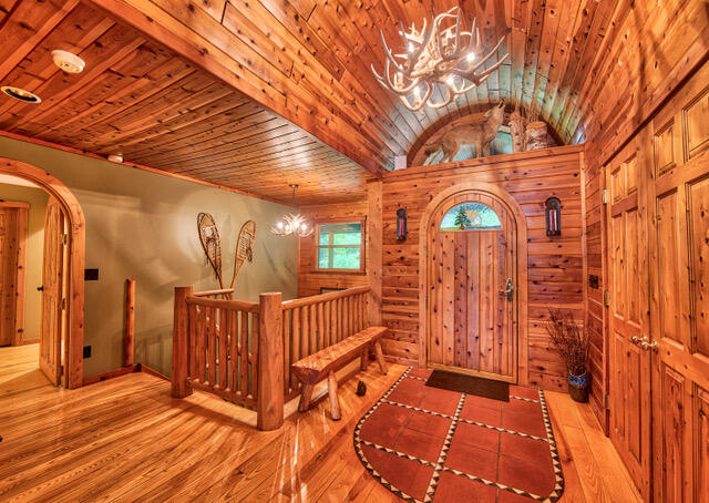 foyer entrance with light hardwood / wood-style floors, lofted ceiling, wooden walls, a notable chandelier, and wood ceiling