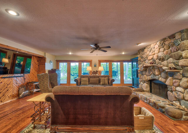 living room with a stone fireplace, ceiling fan, plenty of natural light, and hardwood / wood-style flooring