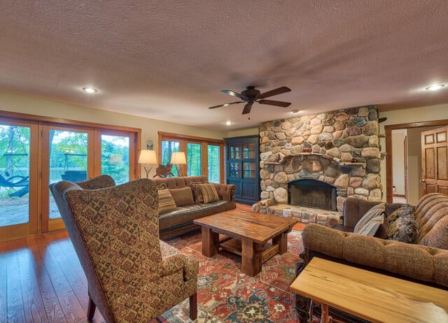 living room with a stone fireplace, ceiling fan, a wealth of natural light, and wood-type flooring