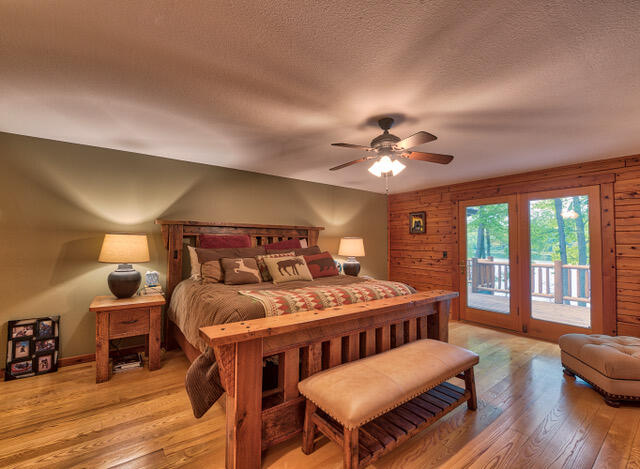 bedroom with wooden walls, ceiling fan, hardwood / wood-style flooring, and access to outside