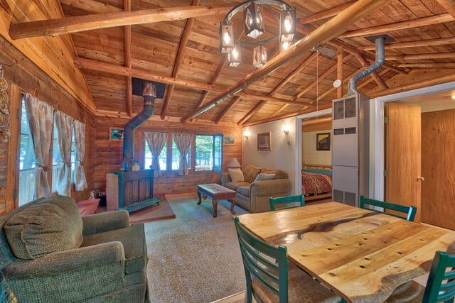 dining area with a wood stove, wooden ceiling, vaulted ceiling with beams, wooden walls, and carpet floors