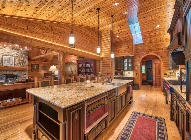 kitchen featuring a center island with sink, sink, log walls, and a skylight