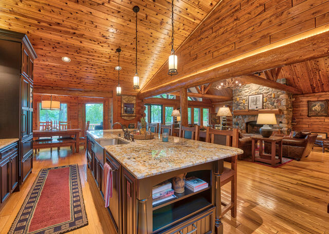 kitchen featuring decorative light fixtures, light hardwood / wood-style floors, a kitchen island with sink, high vaulted ceiling, and log walls