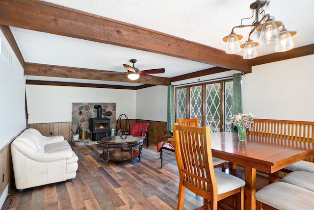 dining space featuring a wood stove, a textured ceiling, ceiling fan with notable chandelier, beamed ceiling, and wood-type flooring