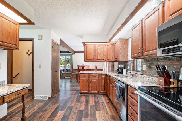 kitchen featuring a textured ceiling, dark wood-type flooring, backsplash, light stone countertops, and appliances with stainless steel finishes