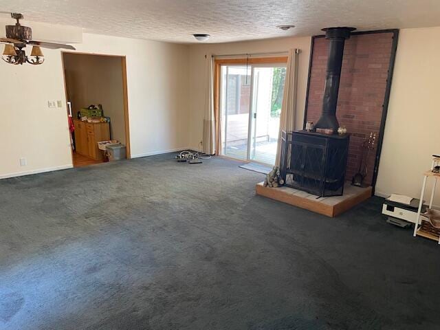 unfurnished living room with brick wall, dark colored carpet, a wood stove, and a textured ceiling