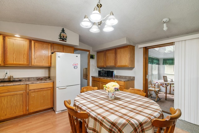 kitchen featuring vaulted ceiling, a textured ceiling, light wood-type flooring, white refrigerator, and pendant lighting