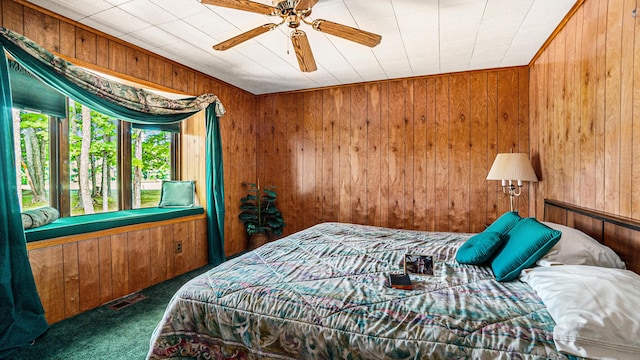 bedroom featuring ceiling fan, wooden walls, and dark carpet