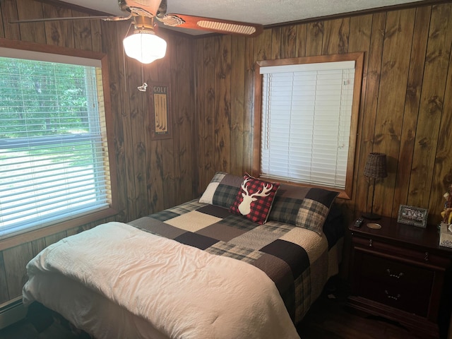 bedroom with a baseboard heating unit, ceiling fan, a textured ceiling, and wood walls