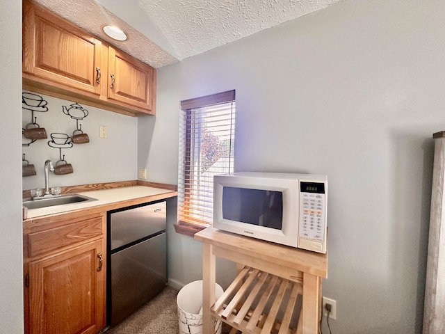 kitchen with a textured ceiling, stainless steel fridge, carpet floors, sink, and lofted ceiling