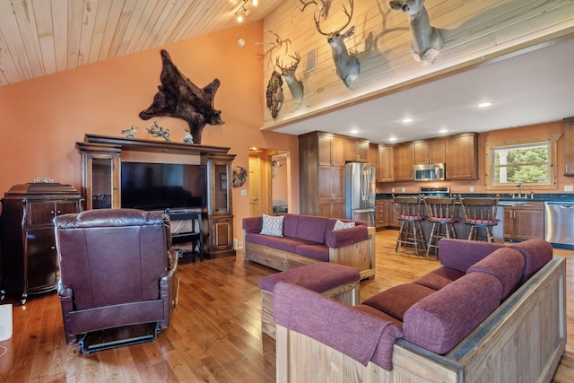 living room with light hardwood / wood-style floors, sink, wooden ceiling, and high vaulted ceiling