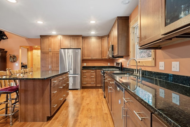 kitchen featuring dark stone counters, a center island, a kitchen bar, appliances with stainless steel finishes, and light hardwood / wood-style flooring