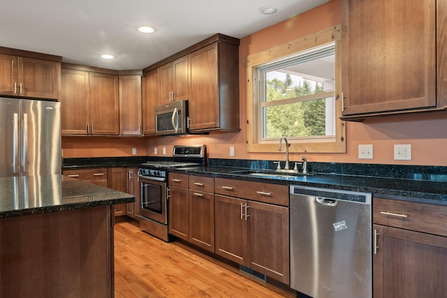 kitchen featuring sink, appliances with stainless steel finishes, dark stone counters, and light hardwood / wood-style flooring