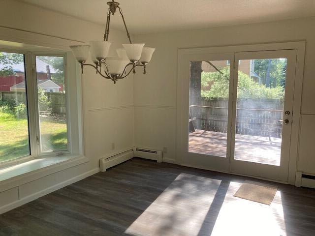 unfurnished dining area with a baseboard heating unit, dark wood-type flooring, and a chandelier