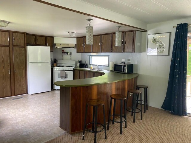 kitchen featuring white appliances, light tile patterned floors, kitchen peninsula, decorative light fixtures, and a kitchen bar