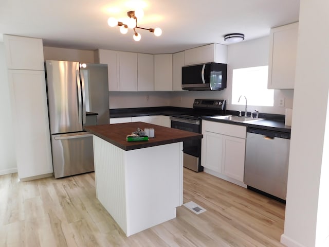 kitchen featuring stainless steel appliances, white cabinets, sink, a center island, and light hardwood / wood-style floors