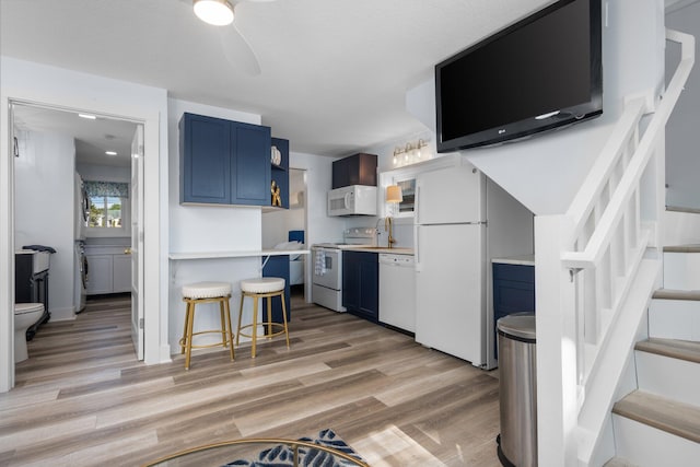 kitchen featuring a breakfast bar, white appliances, light hardwood / wood-style flooring, and blue cabinetry