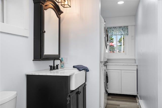 bathroom with hardwood / wood-style floors, vanity, toilet, and stacked washer and dryer