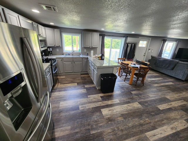 kitchen with dark wood-type flooring, sink, appliances with stainless steel finishes, a kitchen island, and light stone countertops