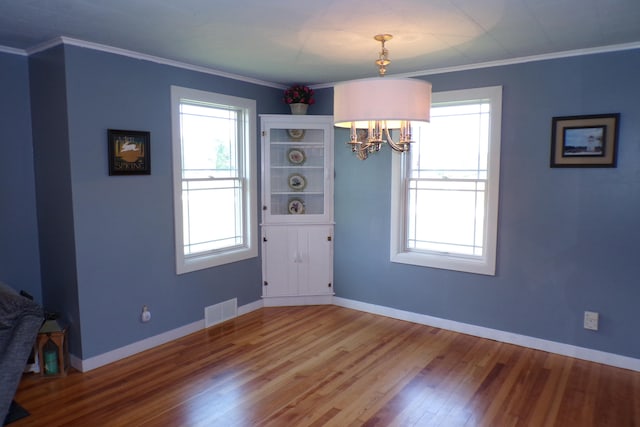 unfurnished dining area featuring wood-type flooring, an inviting chandelier, and crown molding