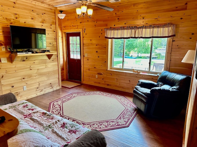 living room featuring wood-type flooring, ceiling fan, and wooden walls