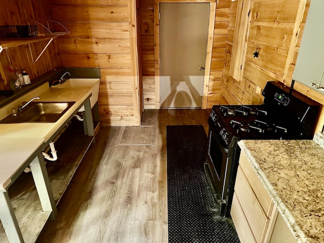 kitchen featuring wood-type flooring, range with gas cooktop, wooden walls, and sink