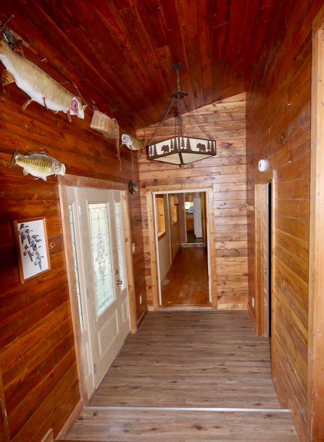 hall with light wood-type flooring, wooden walls, vaulted ceiling, and wooden ceiling